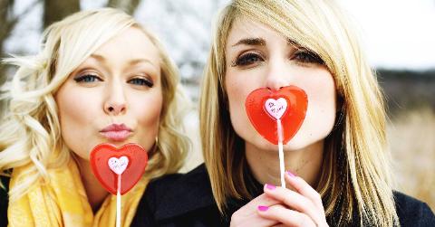 Two sisters both holding up heart-shaped valentine's day lolipops.