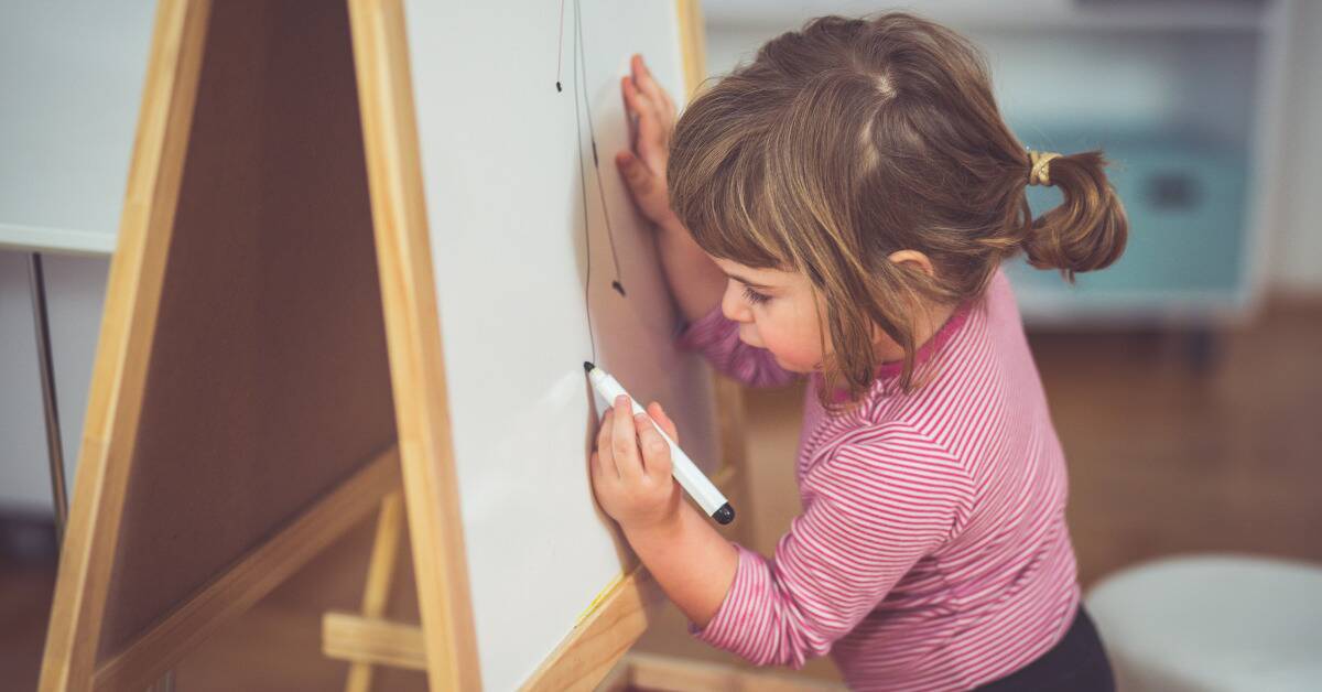 A young girl drawing on a whiteboard with a marker.