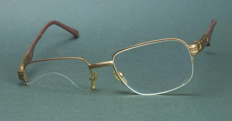 A pair of gold-rimmed glasses with a half-broken lens.