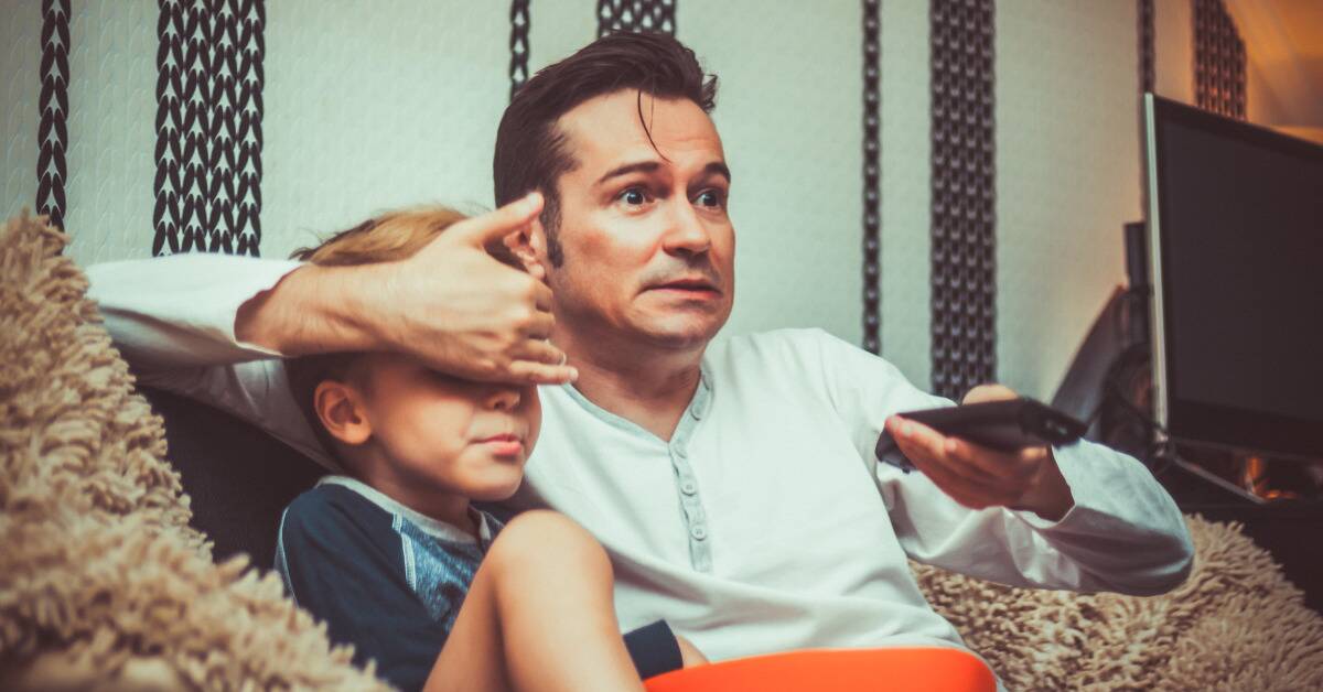 A dad covering his son's eyes as he changes what's on TV.