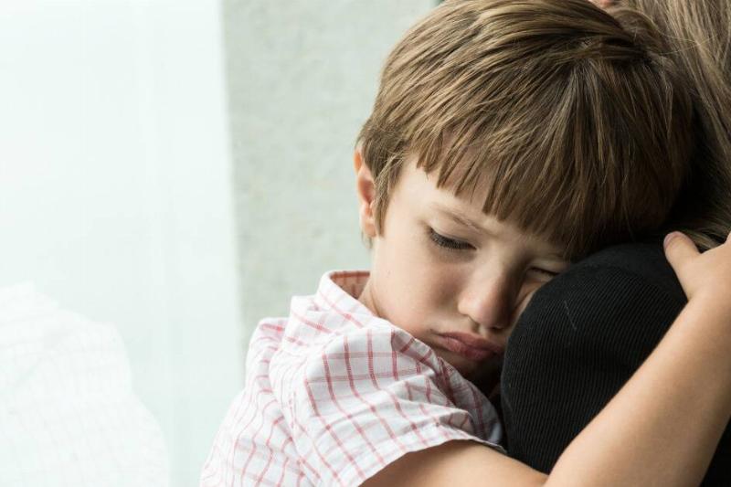 A close shot of a boy sadly hugging his mom's shoulder.