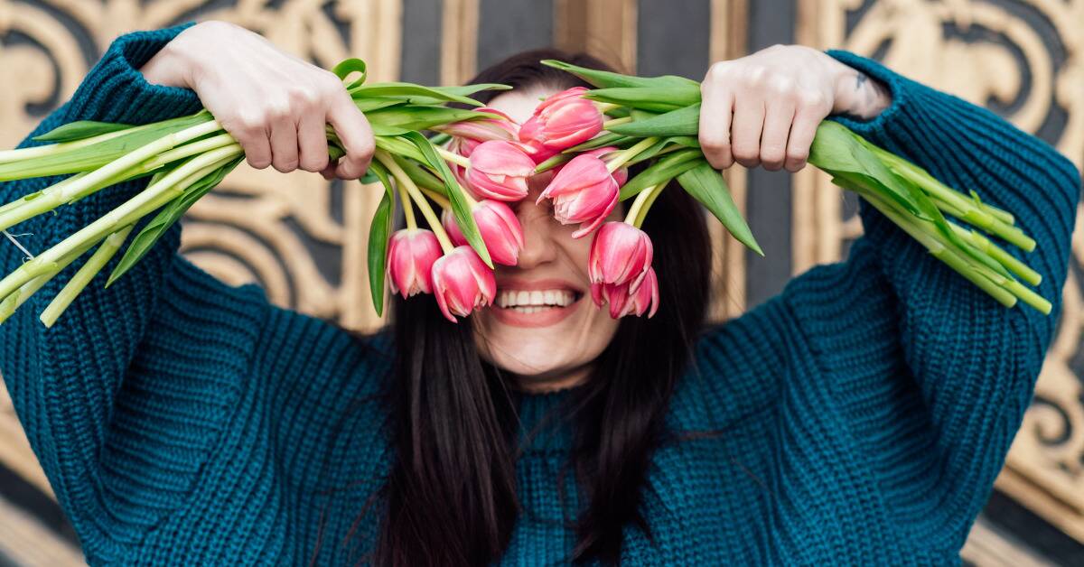 A woman smiling as she holds bundles of pink tulips in front of her eyes.