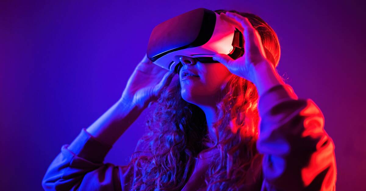 A woman wearing a VR headset lit in dramatic neon lighting.