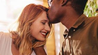 A close shot of a man kissing his girlfriend's forehead, the girlfriend smiling.