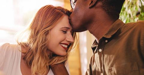 A close shot of a man kissing his girlfriend's forehead, the girlfriend smiling.