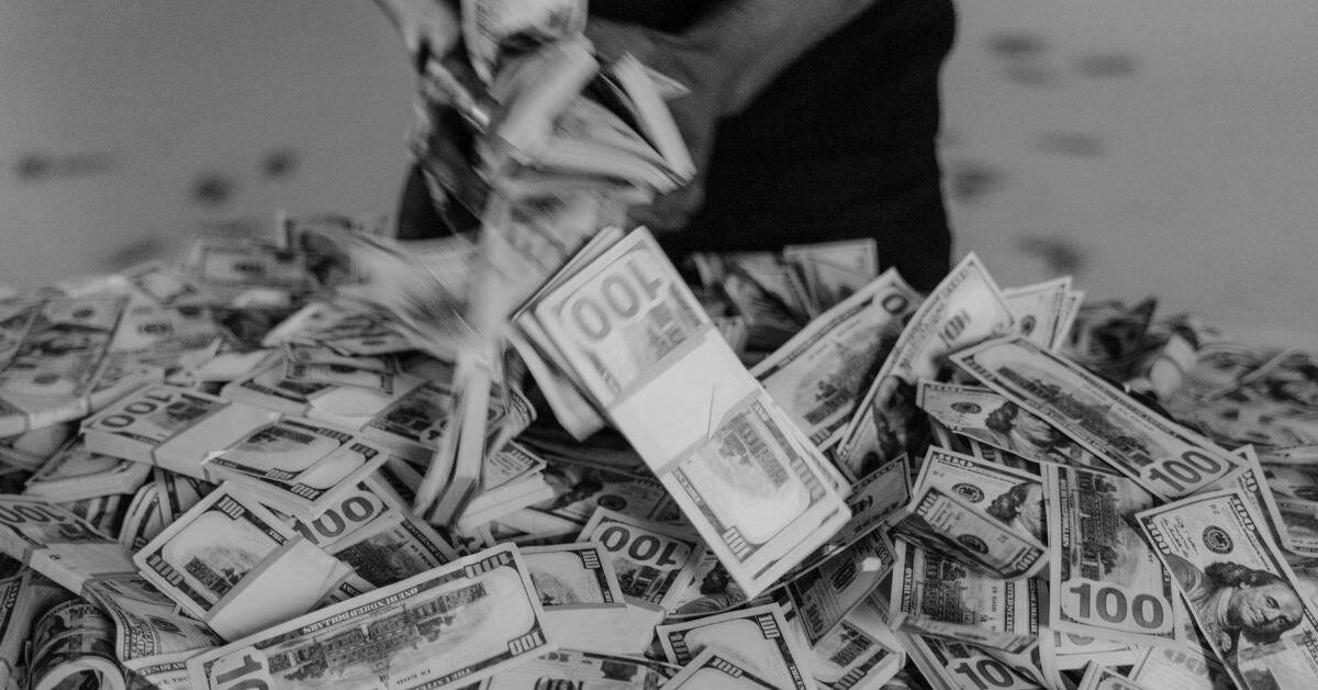 A greyscale image of a man handling stacks of $100 bills.