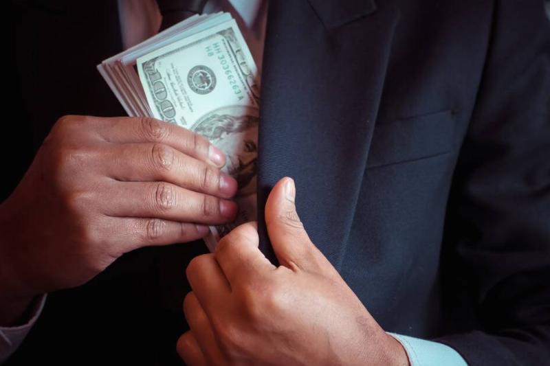 A man tucking a stack of $100 bills into his suit jacket.