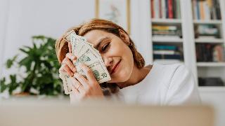 A woman smiling as she rubs a stack of $10 bills on her face.