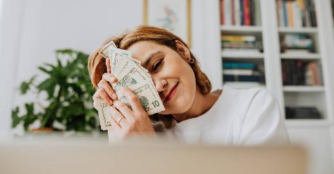 A woman smiling as she rubs a stack of $10 bills on her face.