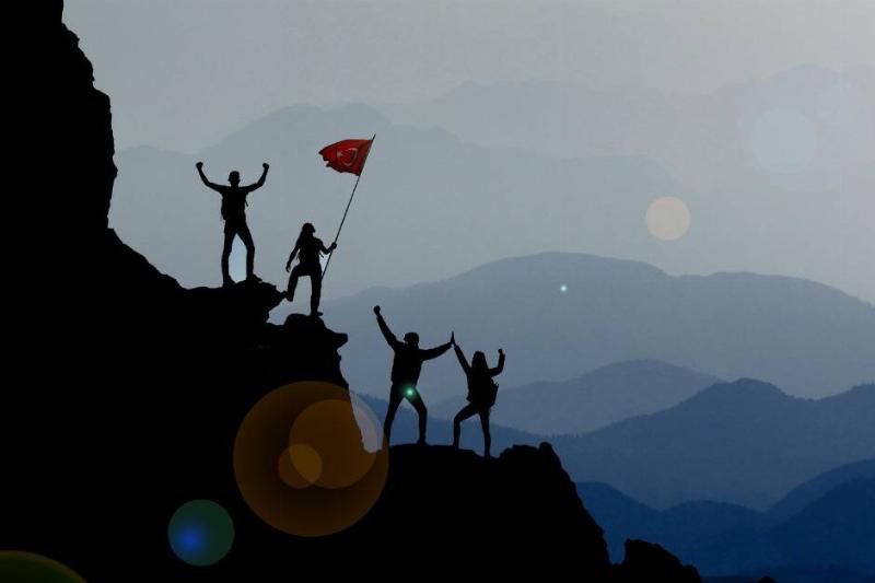 The silhouette of a group of climbers all cheering and waving a flag at the summit of their climb.