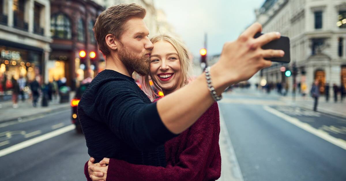 A couple hugging and taking a selfie as they stand in the middle of the street.