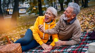 A couple laughing as they lay on a picnic blanket in a park, blowing bubbles together.