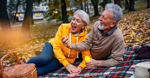 A couple laughing as they lay on a picnic blanket in a park, blowing bubbles together.