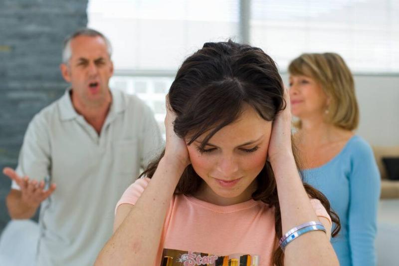 A girl covering her ears as her dad is seen yelling behind her, her mother also there looking disappointed.
