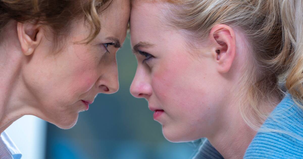 A close shot of a mother and daughter with their foreheads pressed together, both looking into each others' eyes angrily.