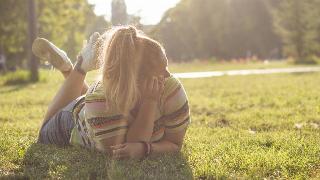 A woman laying on her stomach in the grass, resting her cheek on her hand, legs folded up.