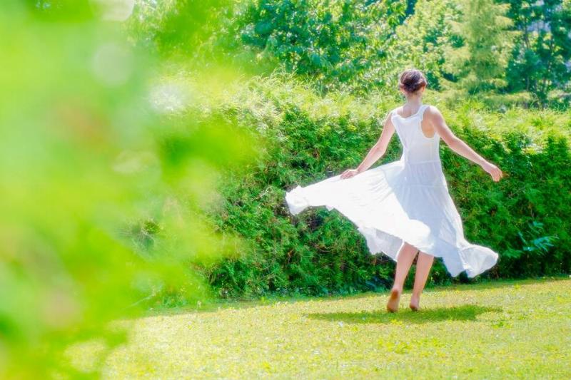 A woman in a flowing white dress walking through a bright green field.