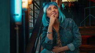 A woman with bright blue hair sitting on a staircase otuside, looking up to the sky with a hopeful expression.
