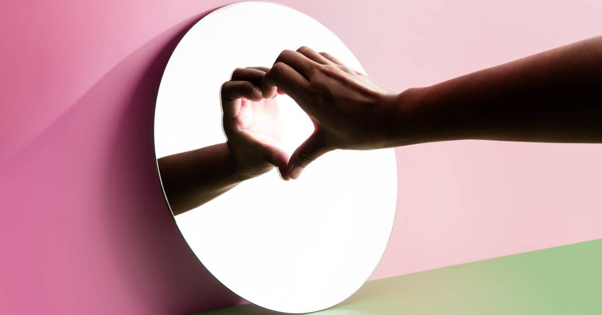 A hand being held up to a mirror in a heart shape.