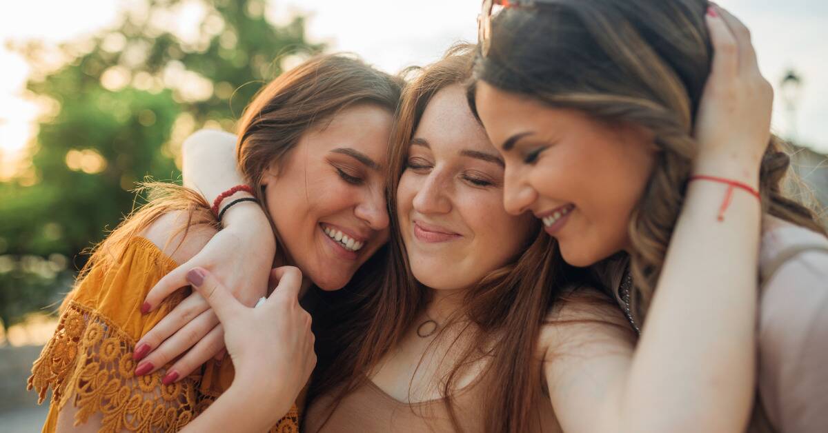 Three friends hugging, their faces close together, all smiling.