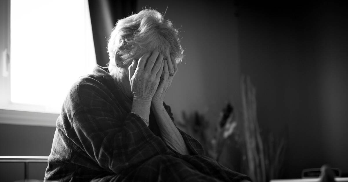 A greyscale image of a woman with her face in her hands.