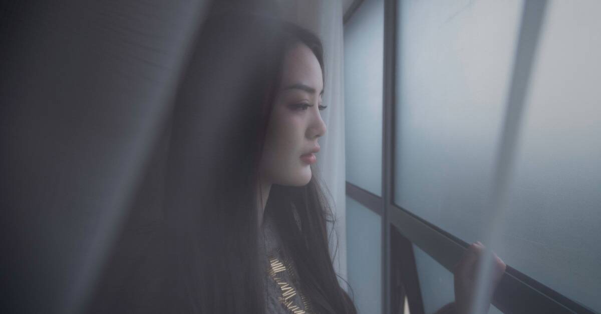 A somber image of a woman looking out a window.