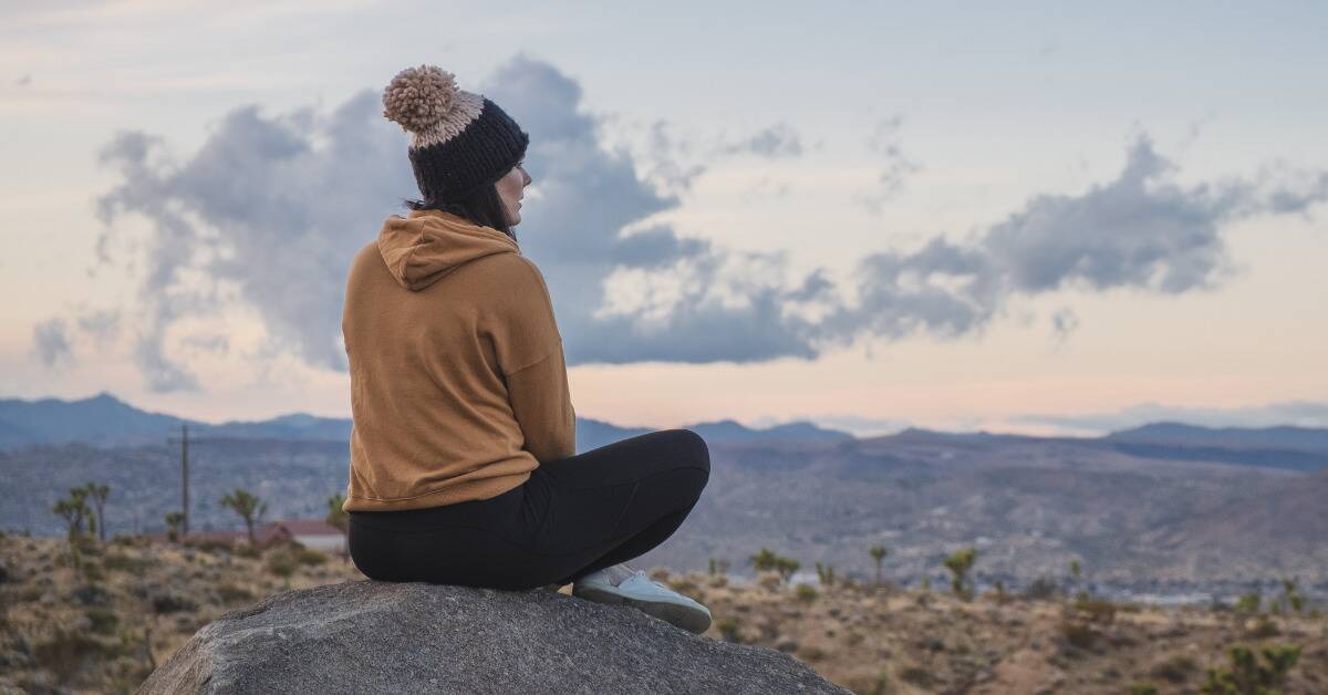 A woman sitting on a rock overlooking the plains.