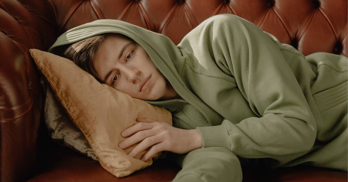 A boy laying down on a couch, looking bored.