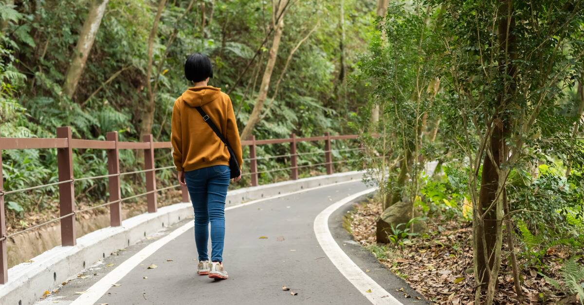 A woman walking down a paved path lined with trees.