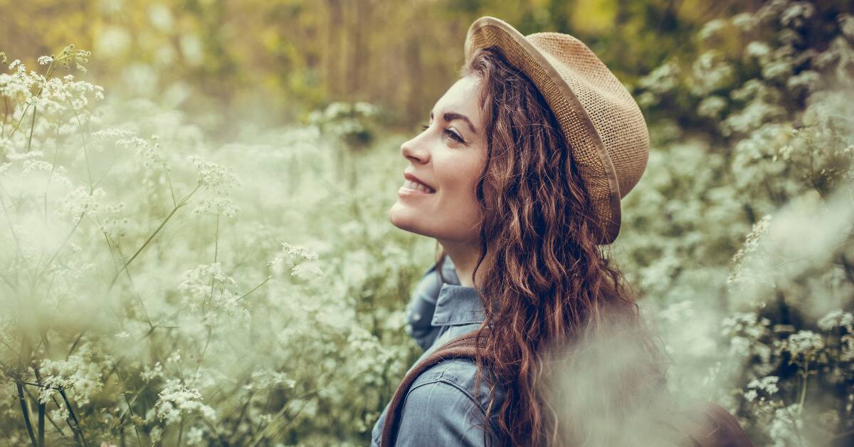 A woman walking through wildflowers, smiling peacefully.