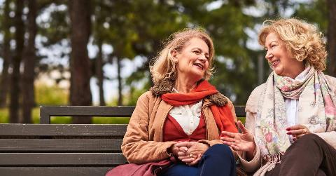 Two friends smiling as they sit and chat on a bench.