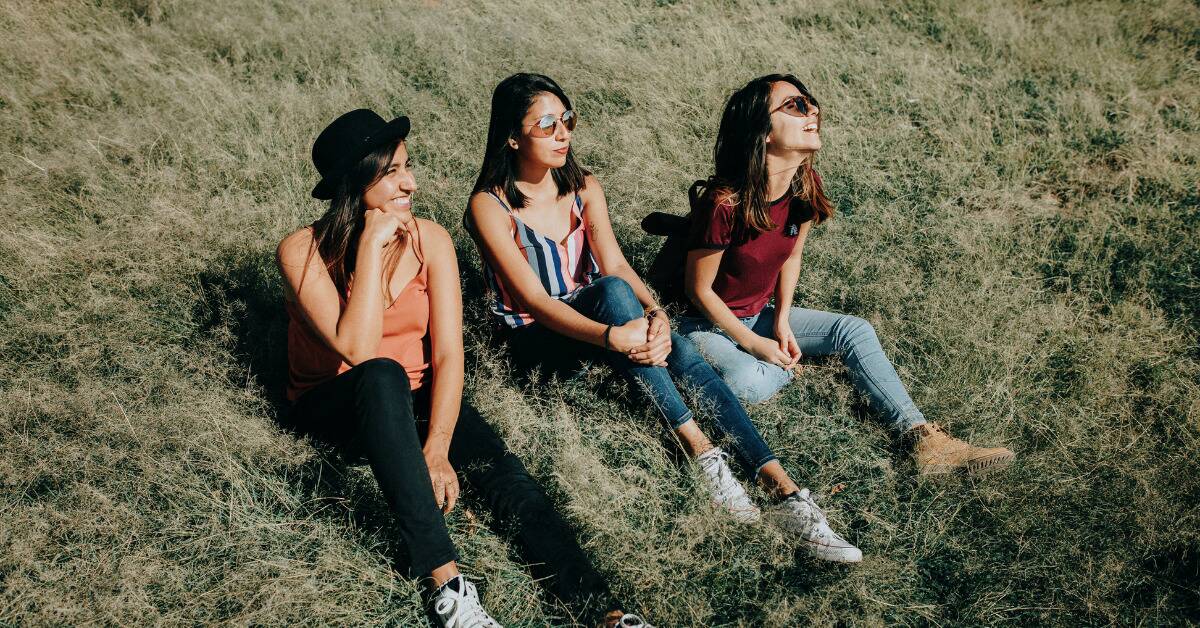 Three friends sitting next to one another on a grassy hill.