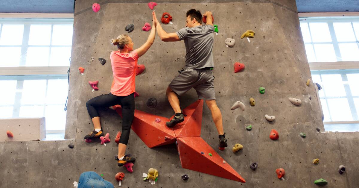 A couple at the top of an indoor rock climbing wall, high-fiving.