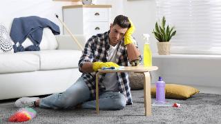 A man sitting on the floor as he wipes a table, looking bored.