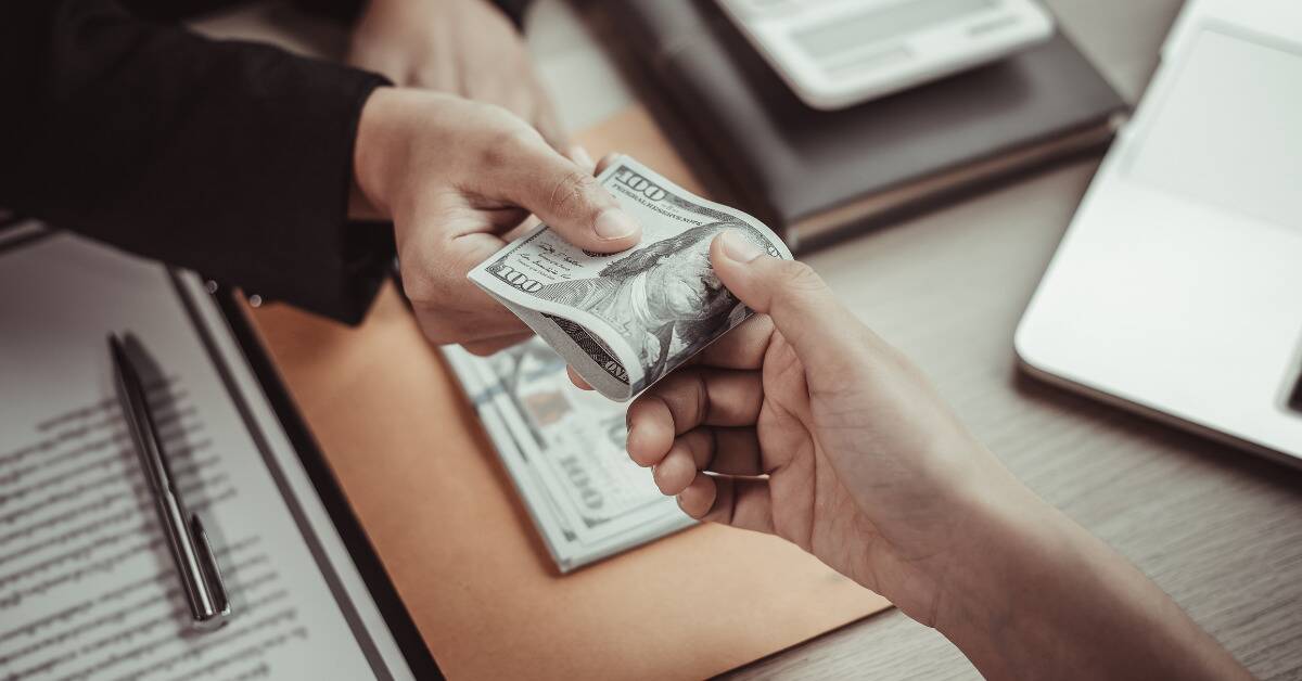 A $100 bill being passed hands over a desk.