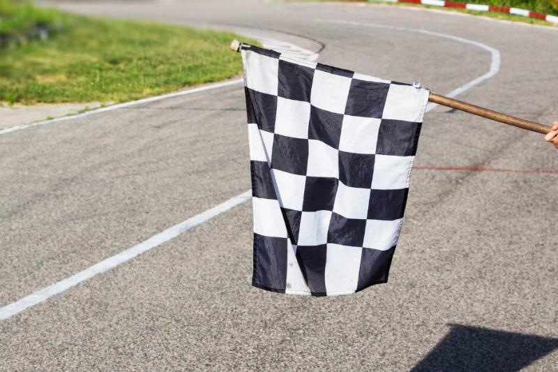 A checkered flag being held a few feet above a paved track.
