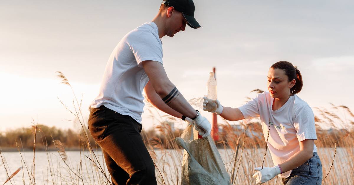 Two people helping pick up garbage around a body of water.