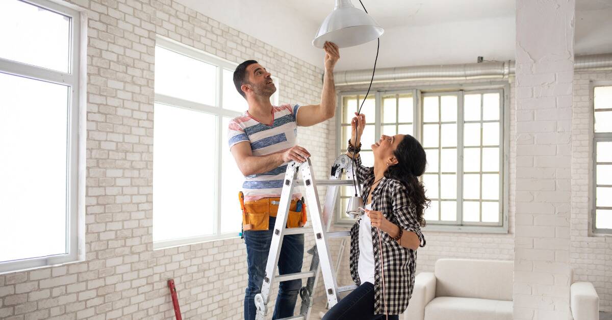 A couple holding up a prospective lighting choice to their ceiling while renovating their home.