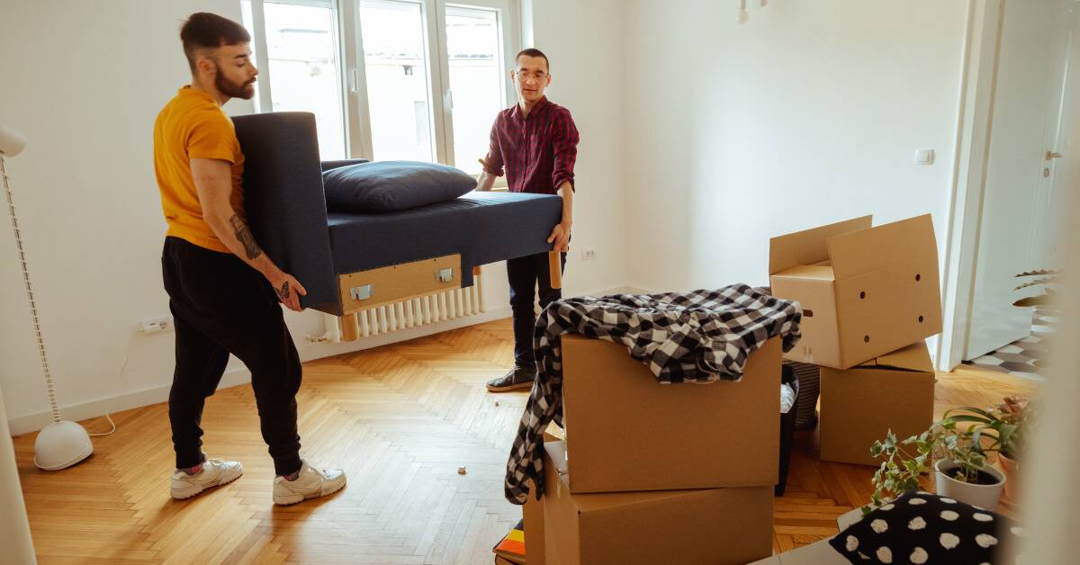 Two men lifting and moving part of a sectional as they move in.