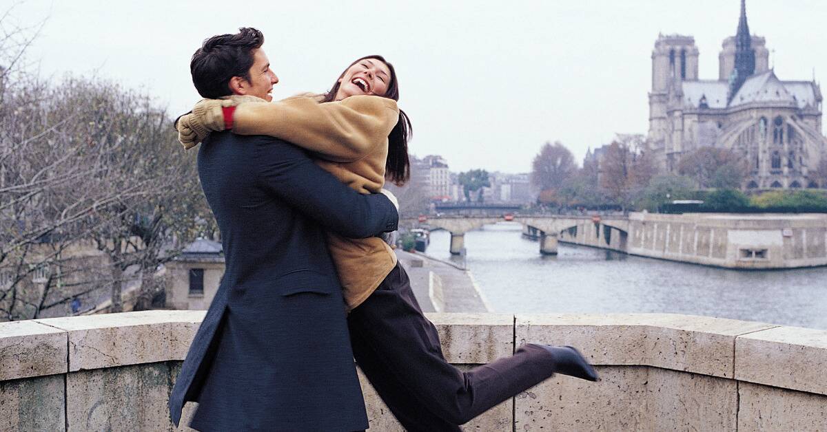 A couple standing outside, hugging, the man swinging the woman in a circle, both smiling.