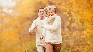 A couple running through an autumn scene, laughing.