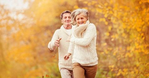 A couple running through an autumn scene, laughing.