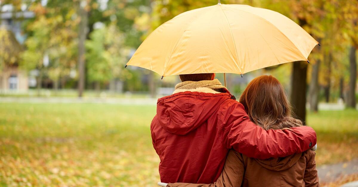 A couple facing away from the camera walking in the rain, holding a yellow umbrella.