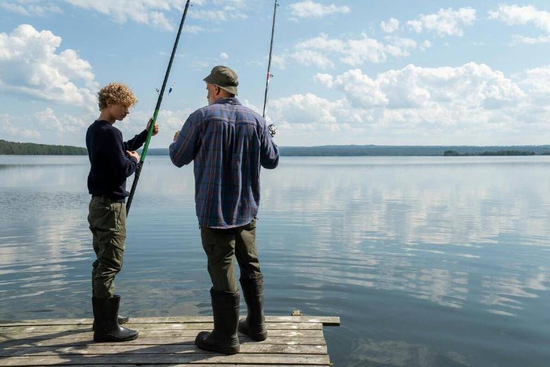 A father teaching his son how to fish on a pier.
