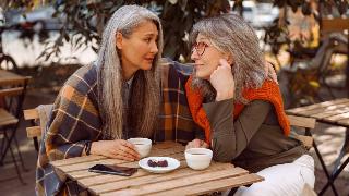 Two women sitting at a cafe, looking into each other's eyes with warm expressions.