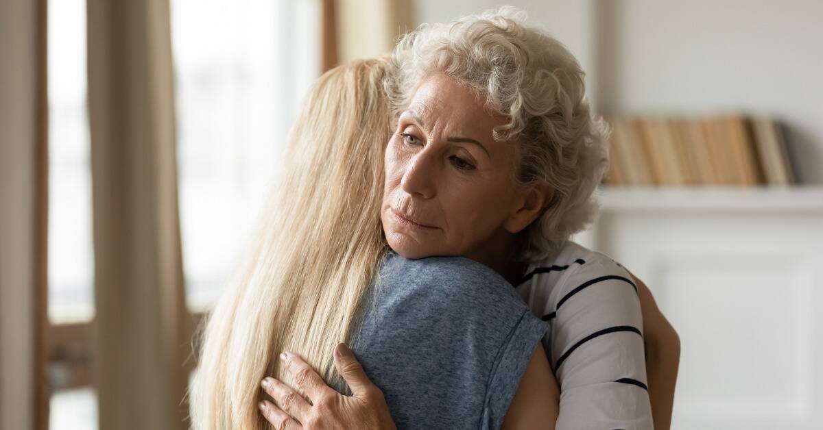 A woman hugging another woman, looking concerned.