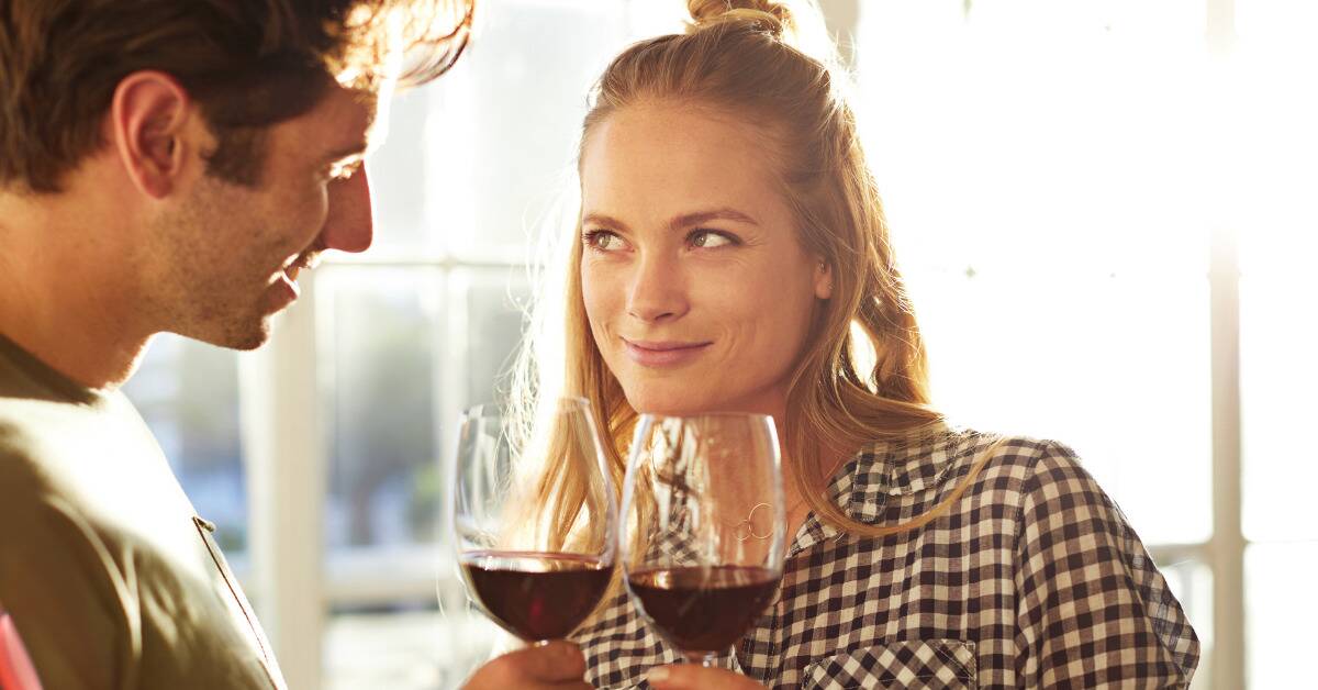 A woman looking at a man with a playful tone as they chat over glasses of wine.