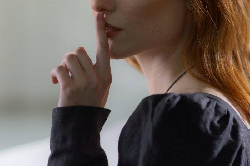 A close shot of a woman placing a finger to her lips in a 'shh' gesture.