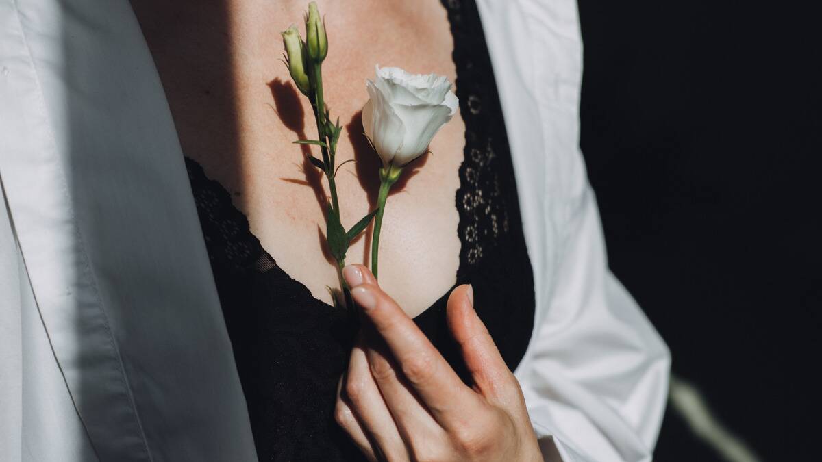 A woman holding a white rose to her chest delicately.