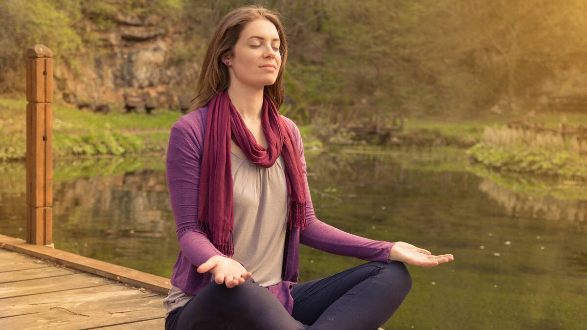 A woman sitting outside by the water, meditating.